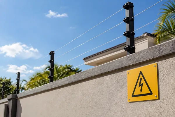 Cerca elétrica instalada sobre muro com placa de advertência